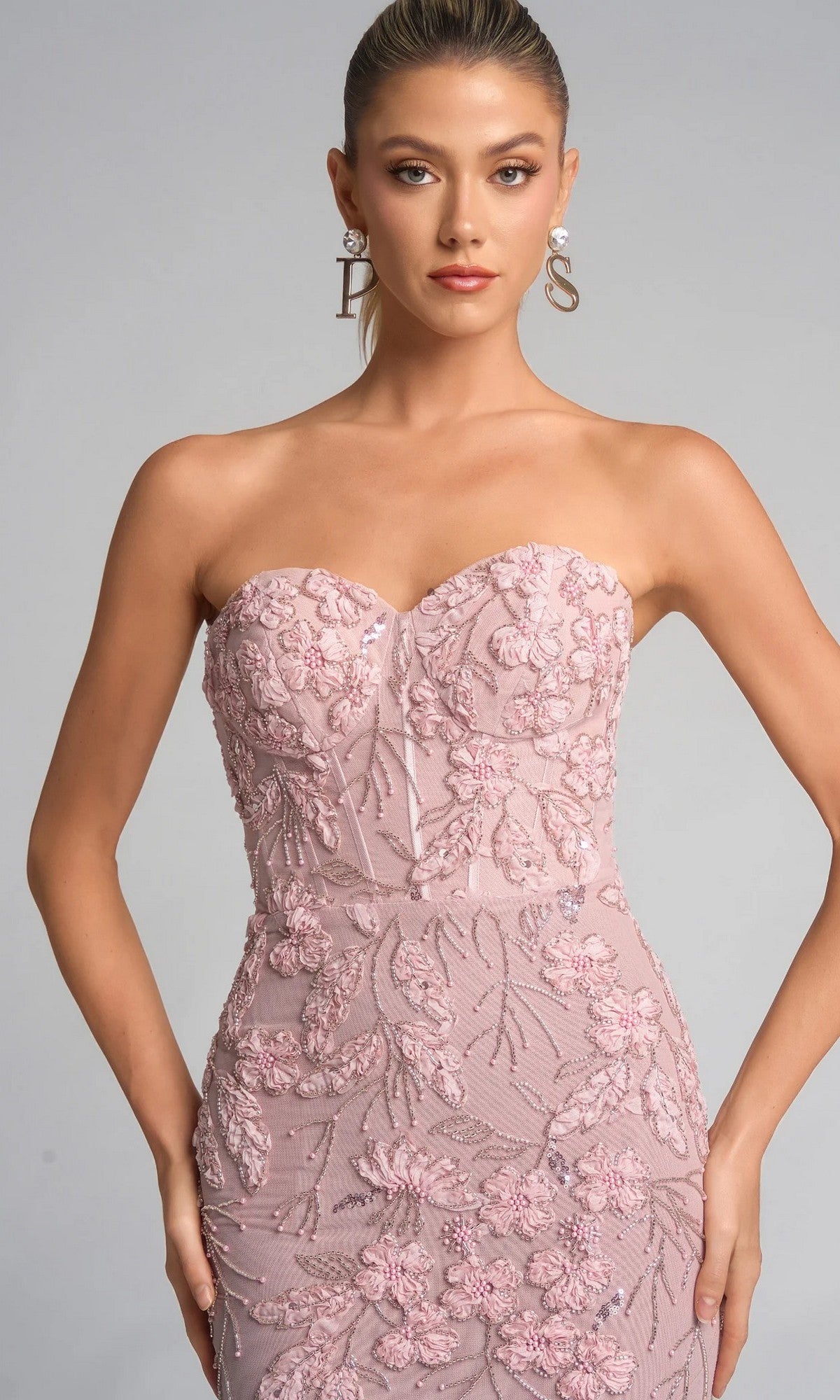 A woman poses against a light gray background wearing the Portia and Scarlett PS26074 long formal dress, featuring a blush pink hue, floral embroidery, strapless sweetheart neckline, and fitted silhouette.